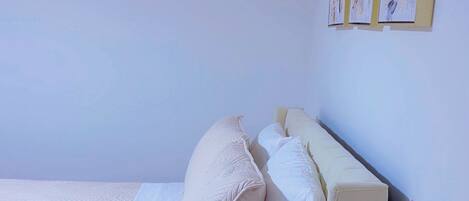 A single bed with a wooden frame and white bedding in a room with light-colored walls and a wooden floor.
