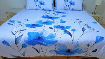 A bed with a floral bedspread and matching pillows, a bedside table with a lamp, and a wooden floor.