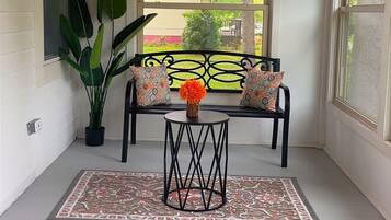 A covered porch with a bench, potted plants, and a view of the outdoors.