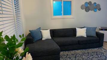 A modern living room with a sectional sofa, a patterned rug, a potted plant, and a wall-mounted light fixture.