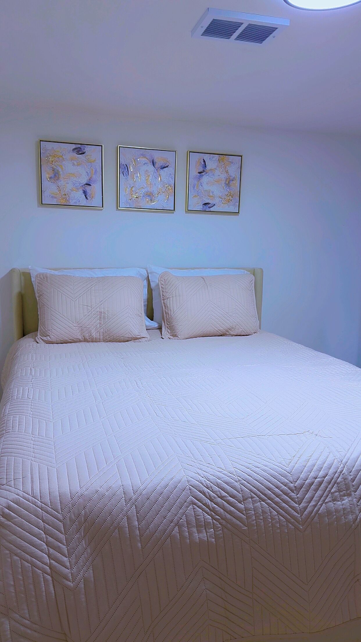 Un dormitorio con una cama, dos almohadas y tres cuadros abstractos en la pared.