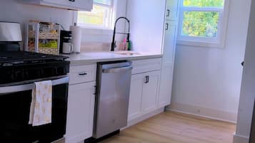 Une cuisine moderne avec des meubles blancs, un four à micro-ondes en acier inoxydable, une cuisinière noire et un lave-vaisselle.