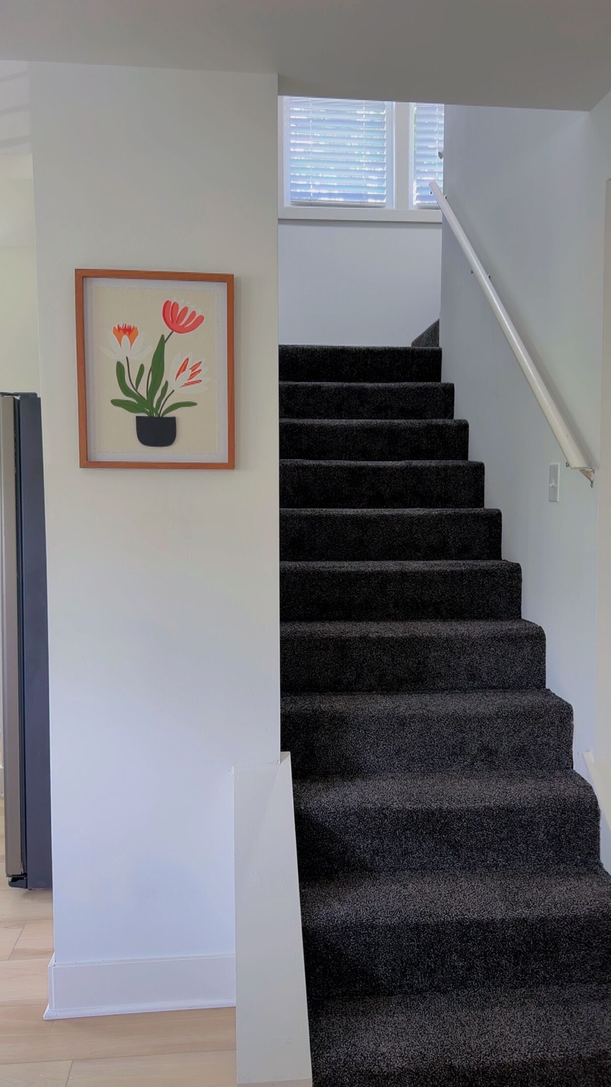 Un escalier muni d’une rampe et d’un tableau représentant des fleurs, accroché au mur.