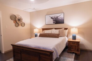 Un dormitorio con cama de madera, dos mesitas de noche con lámparas, una obra de arte colgada en la pared que representa a un toro y adornos decorativos en la pared.
