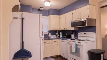 A compact kitchen with white cabinets, a microwave, a stove, and a refrigerator.