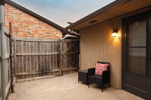A patio area with a wooden fence, a door, and a chair with a cushion. - Cozy 2-bedroom townhome in beautiful Lawton with AC (Lawton)