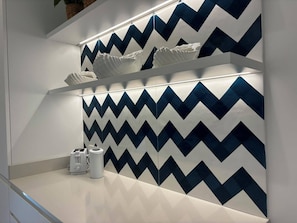 A modern bathroom with a zigzag patterned wall, a white countertop, and a towel rack. - De Vivo Realty - Panorama Suite Sorrento (Sorrento)