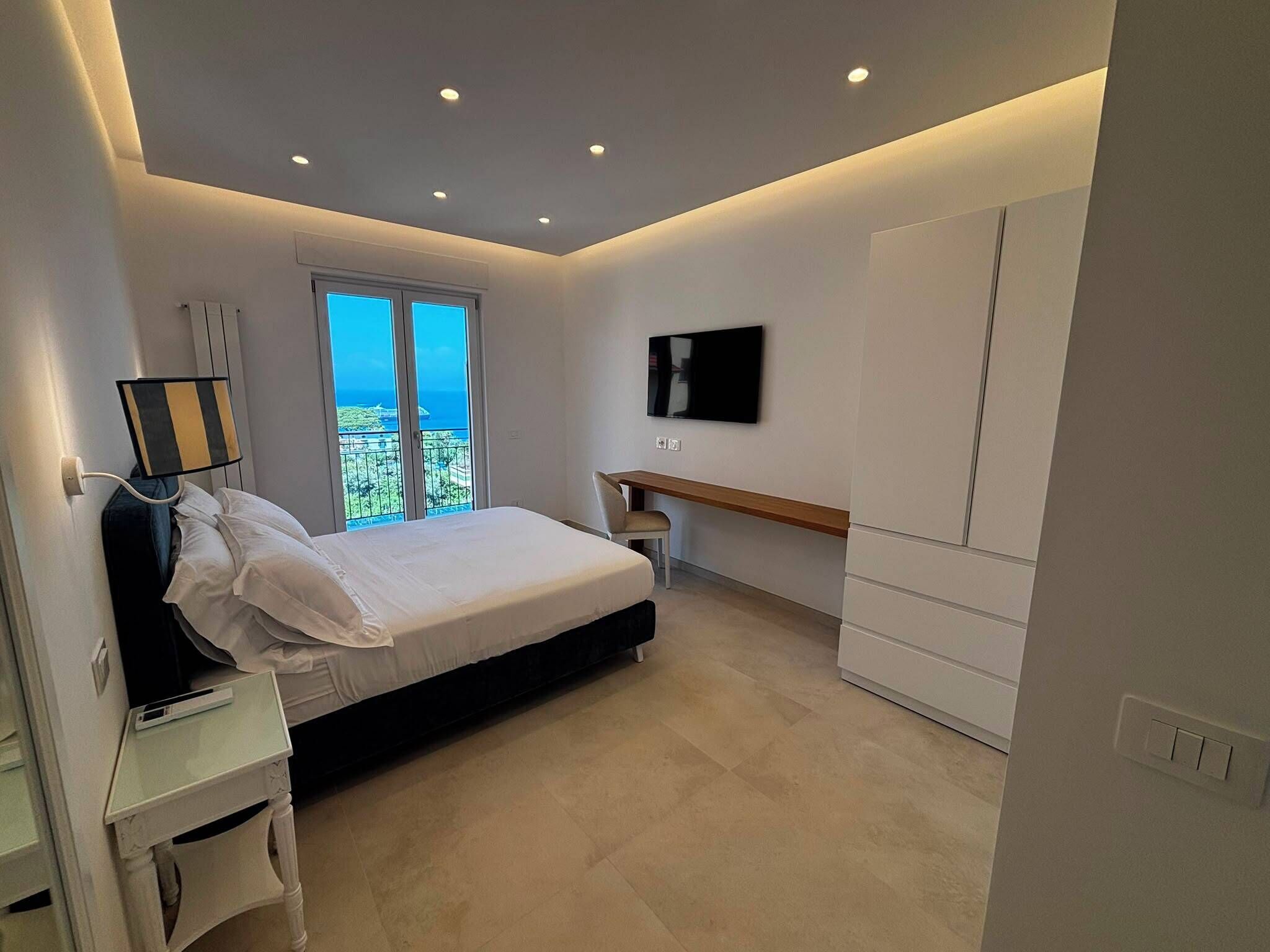 Ein modernes Schlafzimmer mit Bett, Schreibtisch, Sessel, Fernseher und Kleiderschrank.
