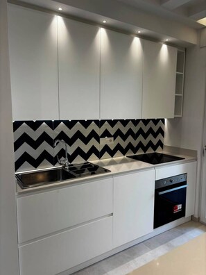 A modern kitchen with built-in cabinets, a black and white backsplash, a stainless steel sink, and a built-in oven. - De Vivo Realty - Panorama Suite Sorrento (Sorrento)