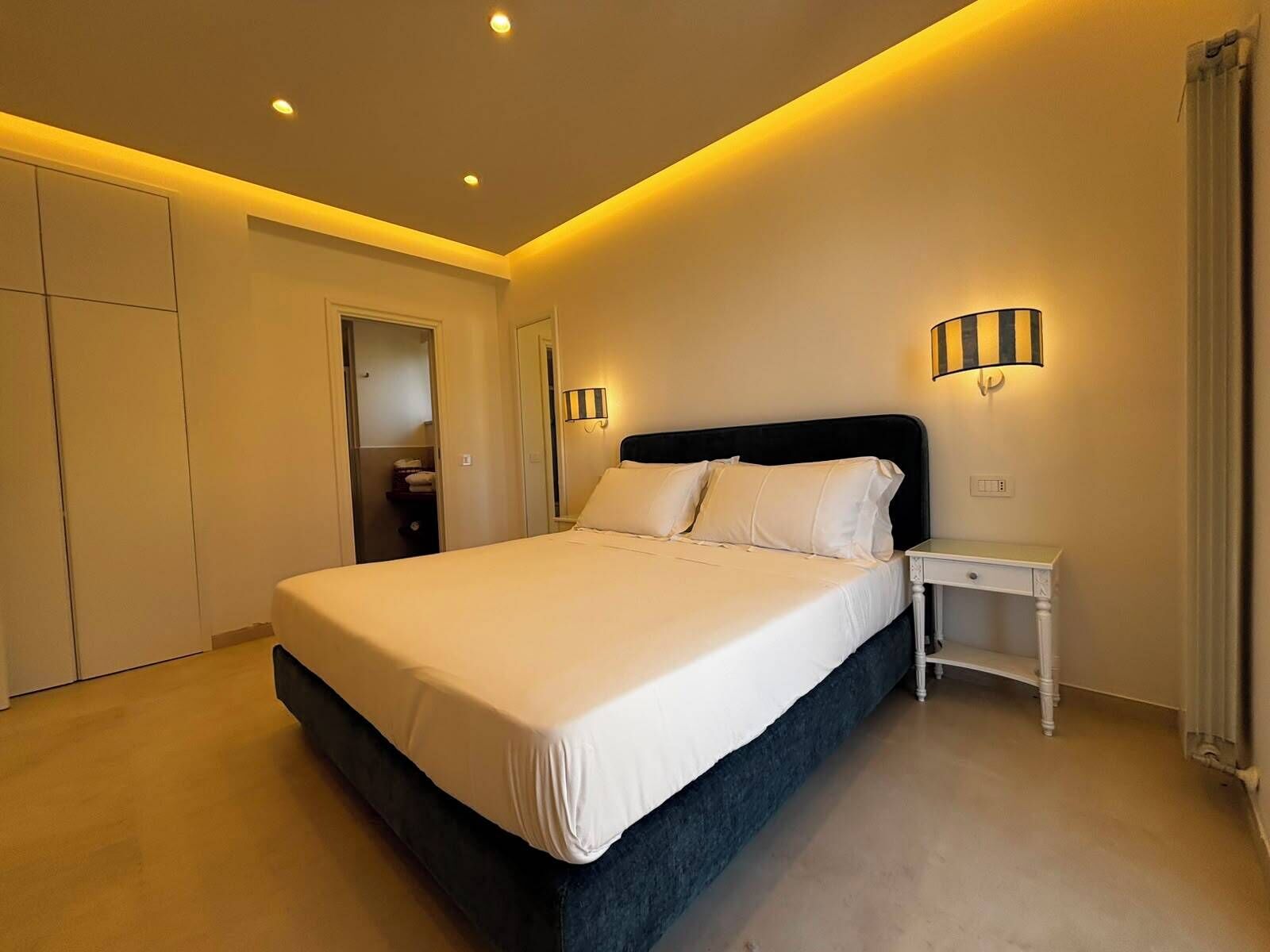 A modern bedroom with a large bed, bedside tables, and a wardrobe.