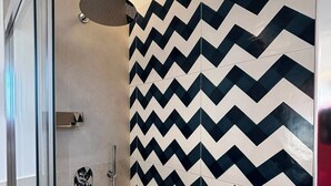 A shower with a black and white chevron tile pattern, a glass door, and a showerhead. - De Vivo Realty - Panorama Suite Sorrento (Sorrento)