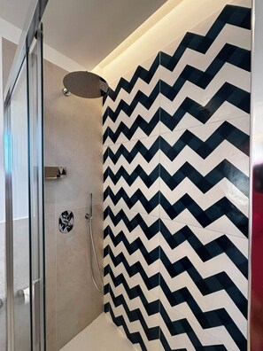 A shower with a black and white chevron tile pattern, a glass door, and a showerhead. - De Vivo Realty - Panorama Suite Sorrento (Sorrento)