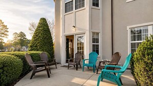 Ein Gebäude mit einer Terrassenanlage, Adirondack-Stühlen und einem gepflegten Heckenstreifen.