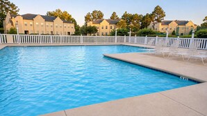 Ein Swimmingpool mit weißer Liegefläche und Liegestühlen, umgeben von einem weißen Zaun und Wohnhäusern.