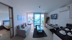 A modern living room with a sofa, a dining table set for two, a television, and a large window offering a view of the city. - Beautifull Condo Apartament With sea View Morros Sonesta (Cartagena)