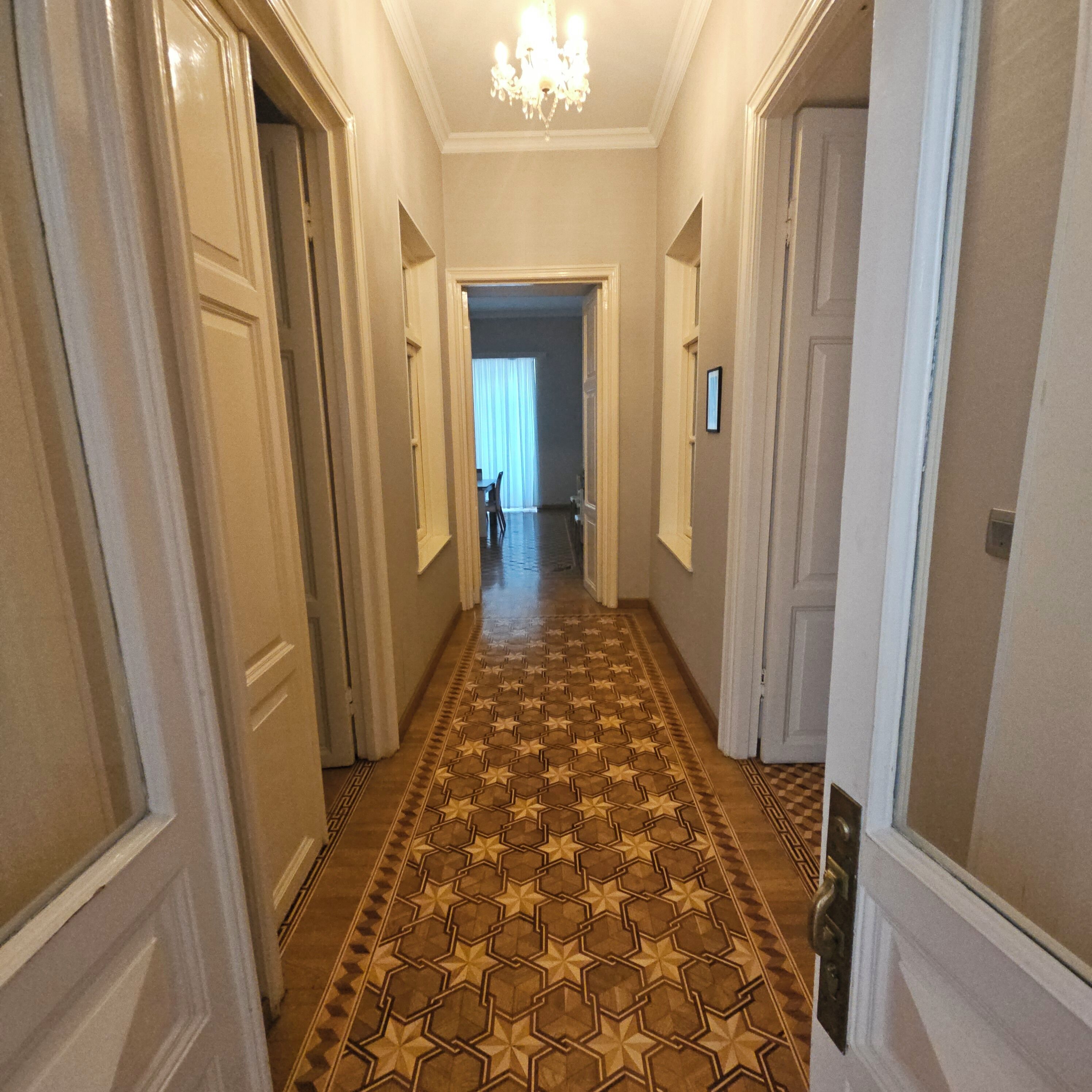 A hallway with patterned flooring, doors on both sides, and a chandelier.