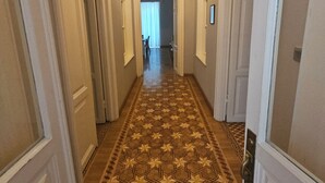 Un pasillo con piso estampado, puertas a ambos lados y un candelabro.