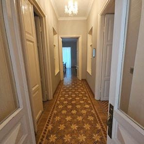 Un pasillo con piso estampado, puertas a ambos lados y un candelabro.