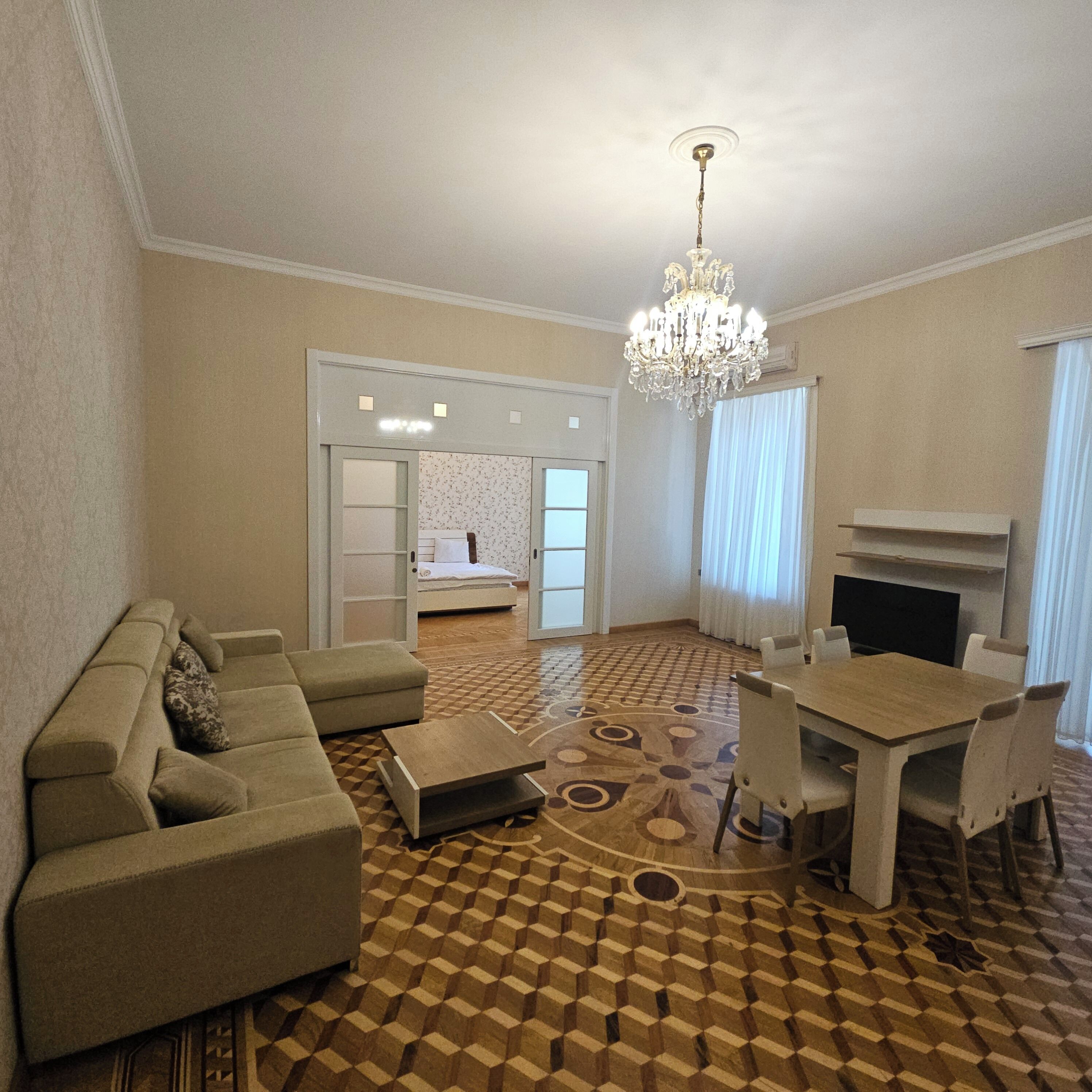 Un salon comprenant un canapé, une table basse, une table à manger avec des chaises, un lustre et une cheminée.