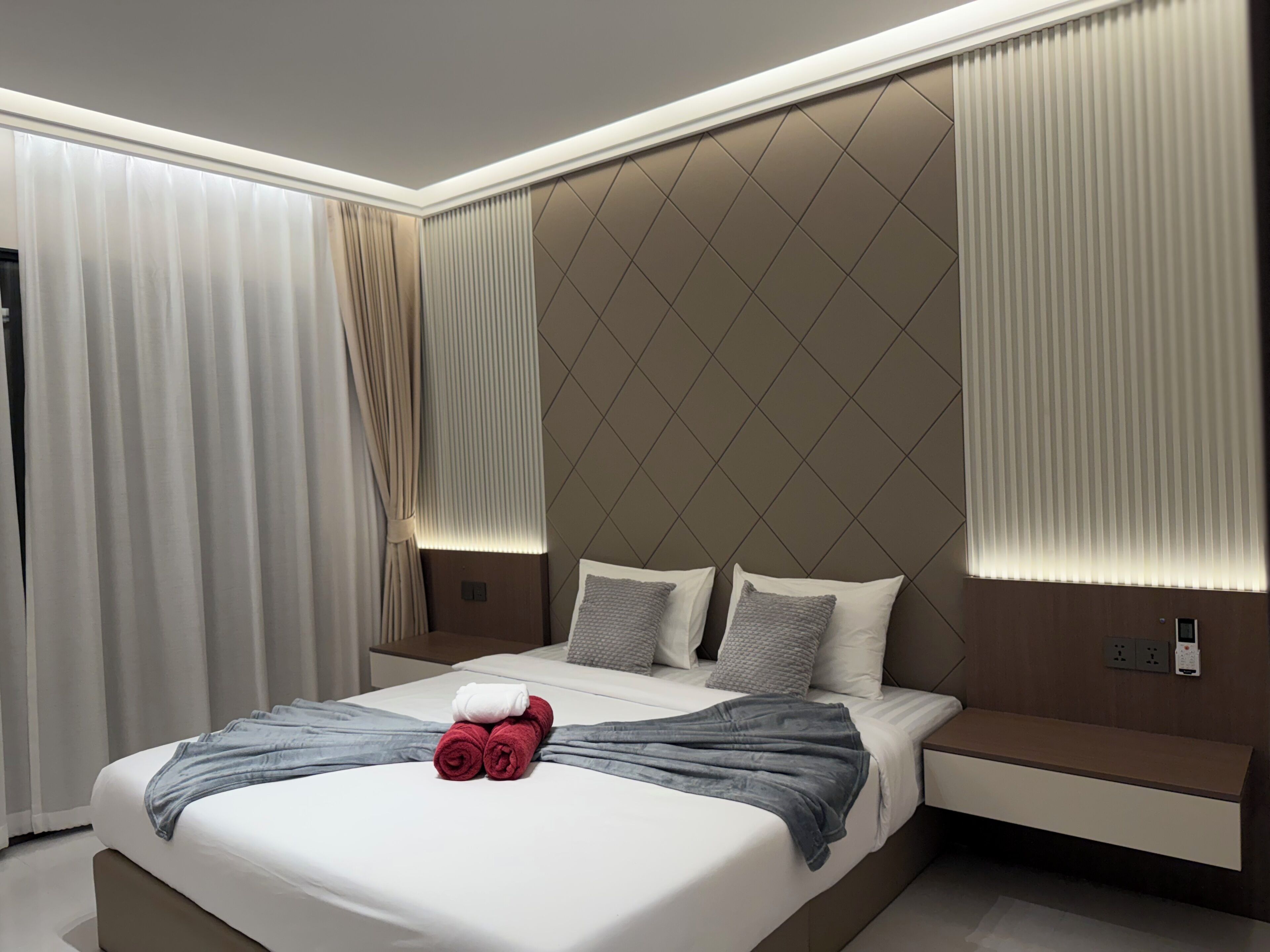 A modern hotel room with a large bed, a bedside table, and a built-in bench.