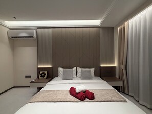 A modern hotel room with a large bed, a bedside table, an air conditioning unit, and a view of the outside through curtains. - Tremendous 6-bedroom house with AC in Bang Lamung District (Bang Lamung District)