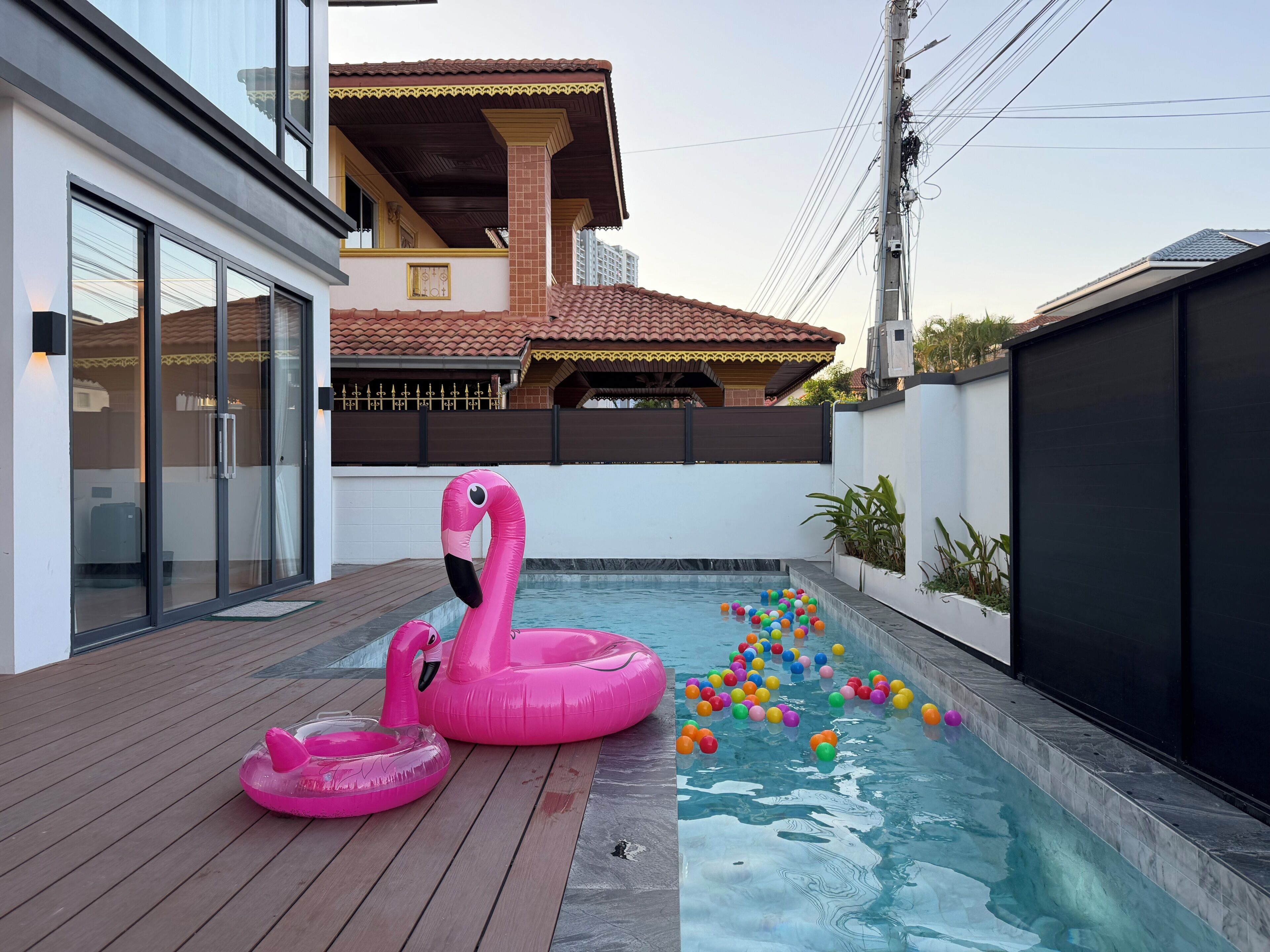 A swimming pool with a wooden deck, a pink flamingo float, and colorful balls.