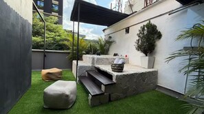 A rooftop patio with artificial grass, a stone bench, and a small seating area. - Luxury Provence Terrace (Medellín)