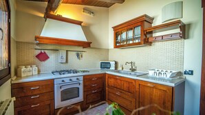 A kitchen with wooden cabinets, a gas stove, a microwave, and a sink. - Sicilian villa with pool 400m above sea level (Avola)