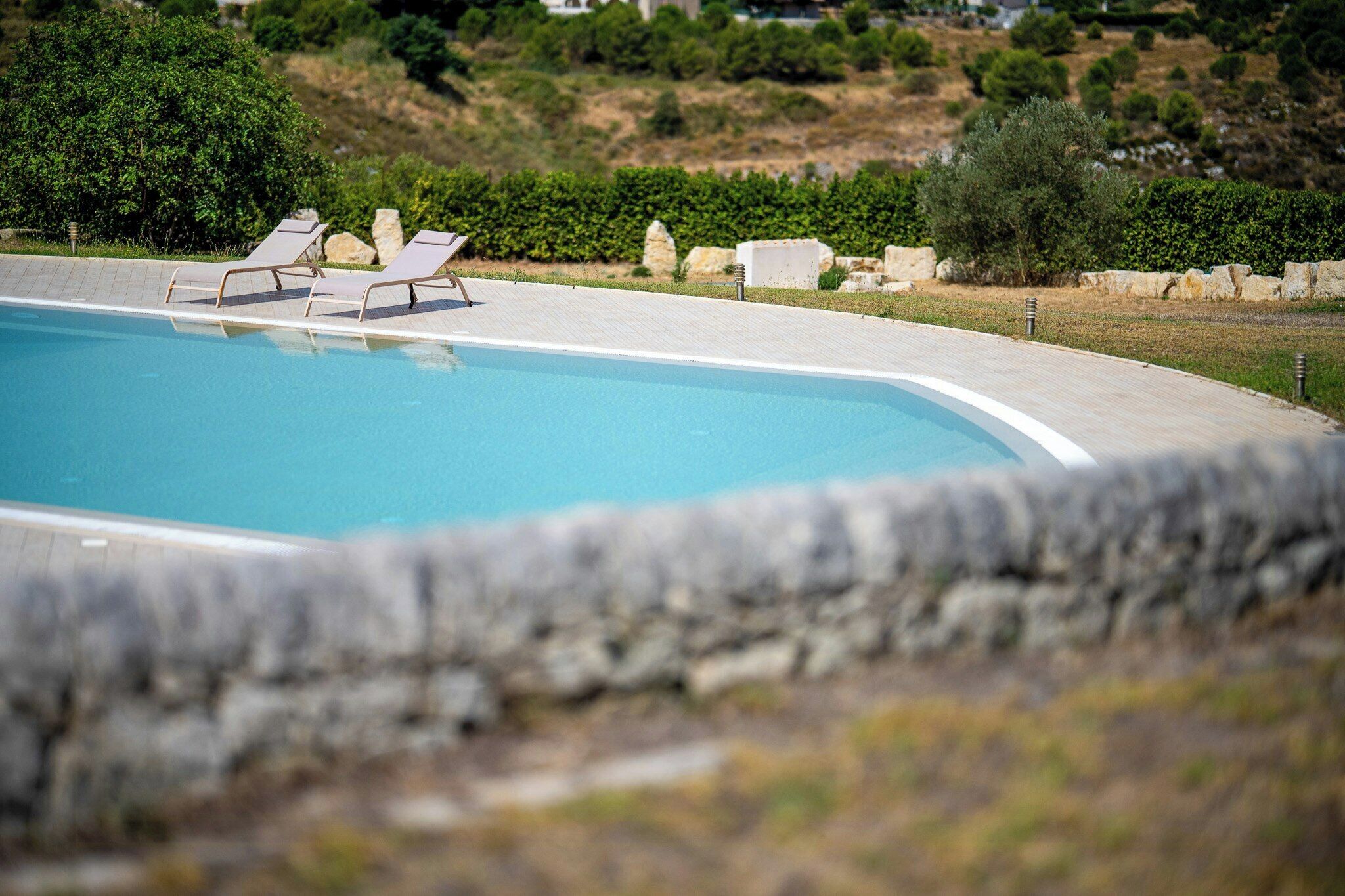 A swimming pool with lounge chairs and a stone wall in the foreground.