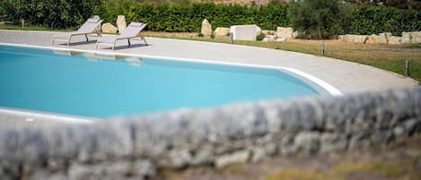 A swimming pool with lounge chairs and a stone wall in the foreground.