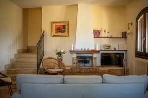 Ein Wohnzimmer mit Kamin, einer Couch, einem Korbsessel und einer Treppe.