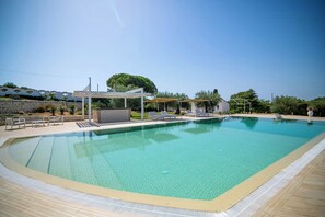 Une piscine rectangulaire à l’eau d’un bleu limpide, entourée d’une terrasse carrelée et de chaises longues.