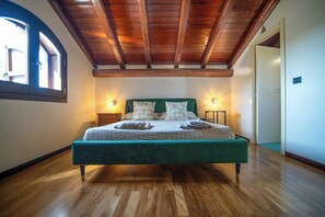 Une chambre avec un plafond en bois, un lit doté d’une tête de lit verte, deux lampes de chevet et une fenêtre sur le côté gauche.