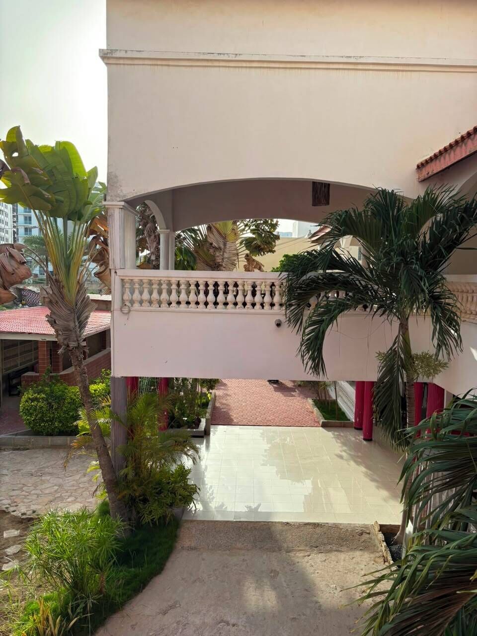 A building with a covered walkway, palm trees, and a red fence.