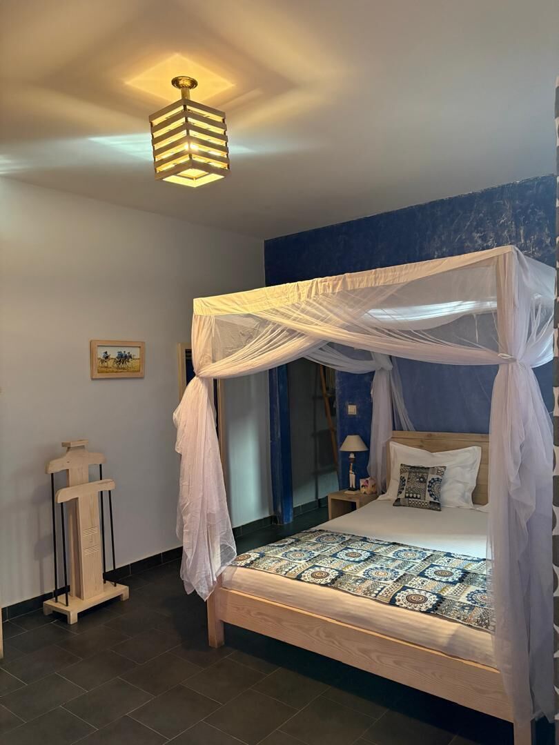 A bedroom with a canopy bed, a bedside table, a lamp, and a wall-mounted light fixture.