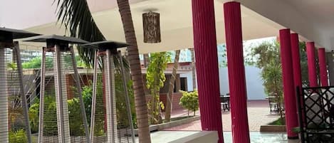 A covered outdoor area with a white balustrade, red pillars, and a view of greenery and buildings in the background.