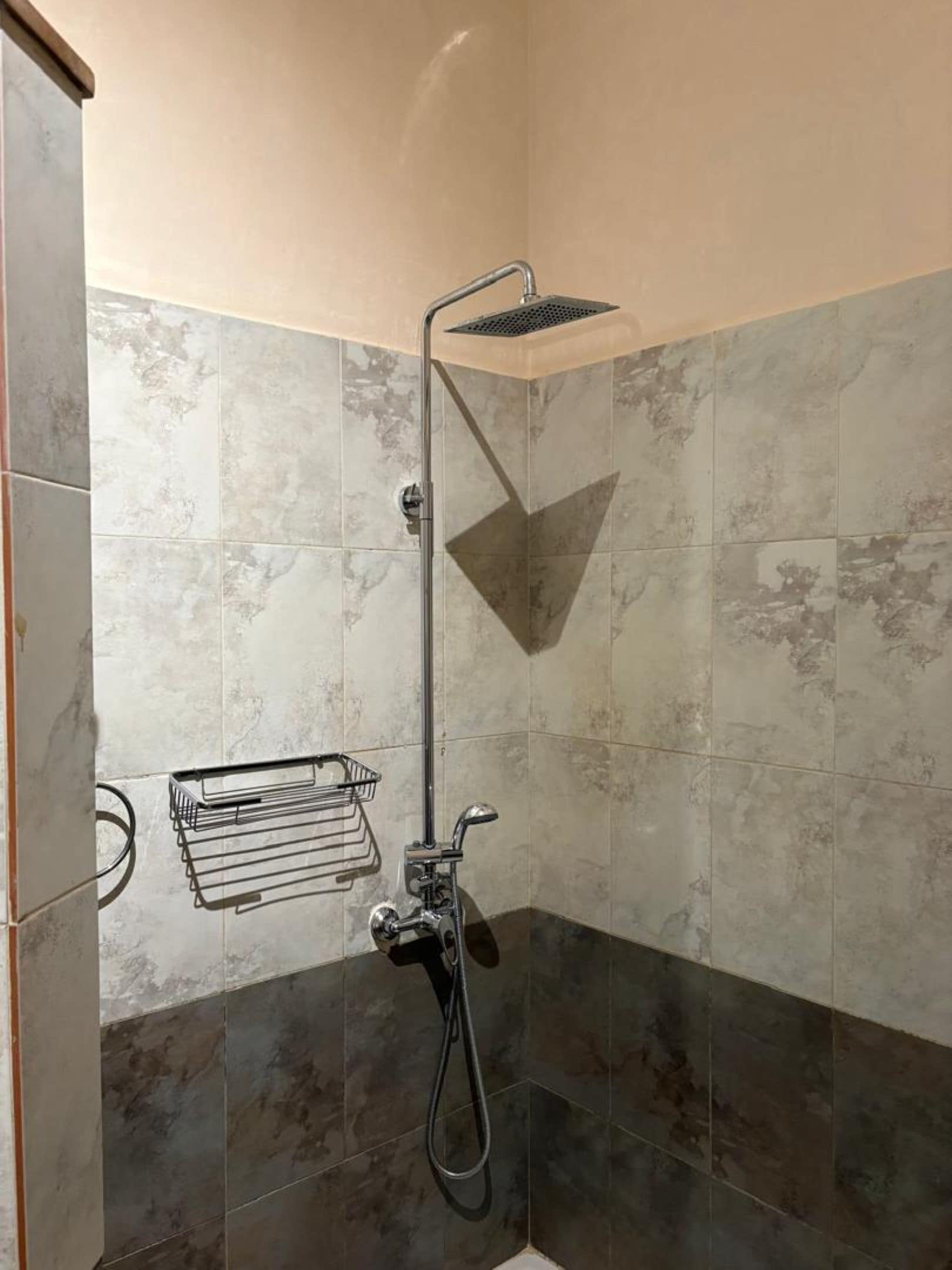 A corner shower with a handheld showerhead, a wall-mounted towel rack, and a corner sink.
