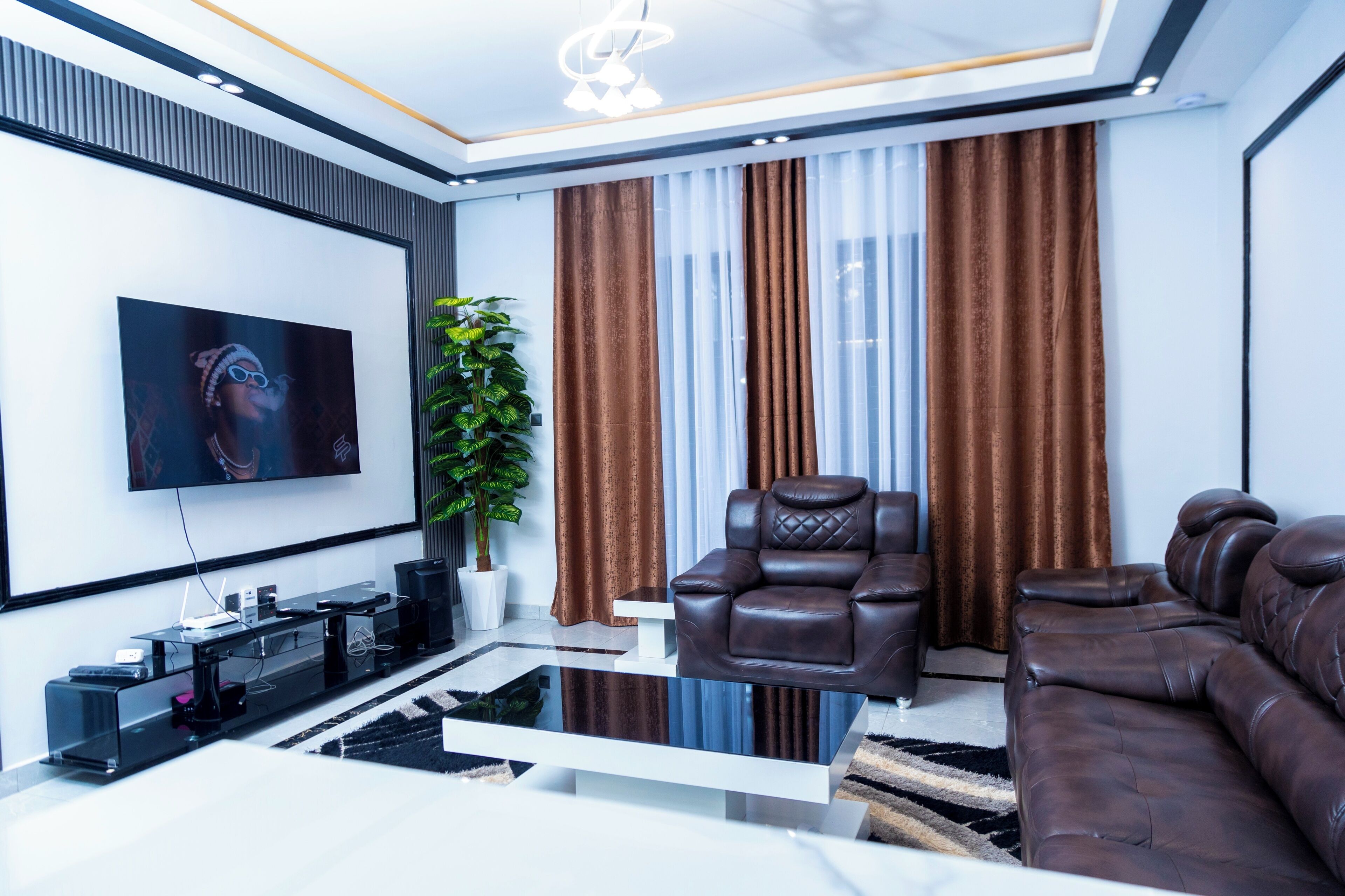 A modern living room with a flat-screen TV, leather recliner, sofa, and a glass coffee table.
