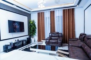 A modern living room with a flat-screen TV, leather recliner, sofa, and a glass coffee table.