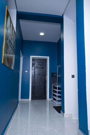 A hallway with a dark door, a white wall, and a blue accent wall. - Luxury 6BR, 5-Bath, Sleeps 12+ – BBB Nation Oasis - Premium Kigali Group Stay (Kigali)