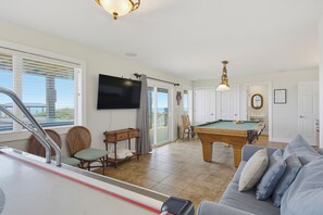 A spacious living area with a pool table, comfortable seating, a television, and a view of the outdoors. - Oceanfront pool and pirate playhouse (North Topsail Beach)