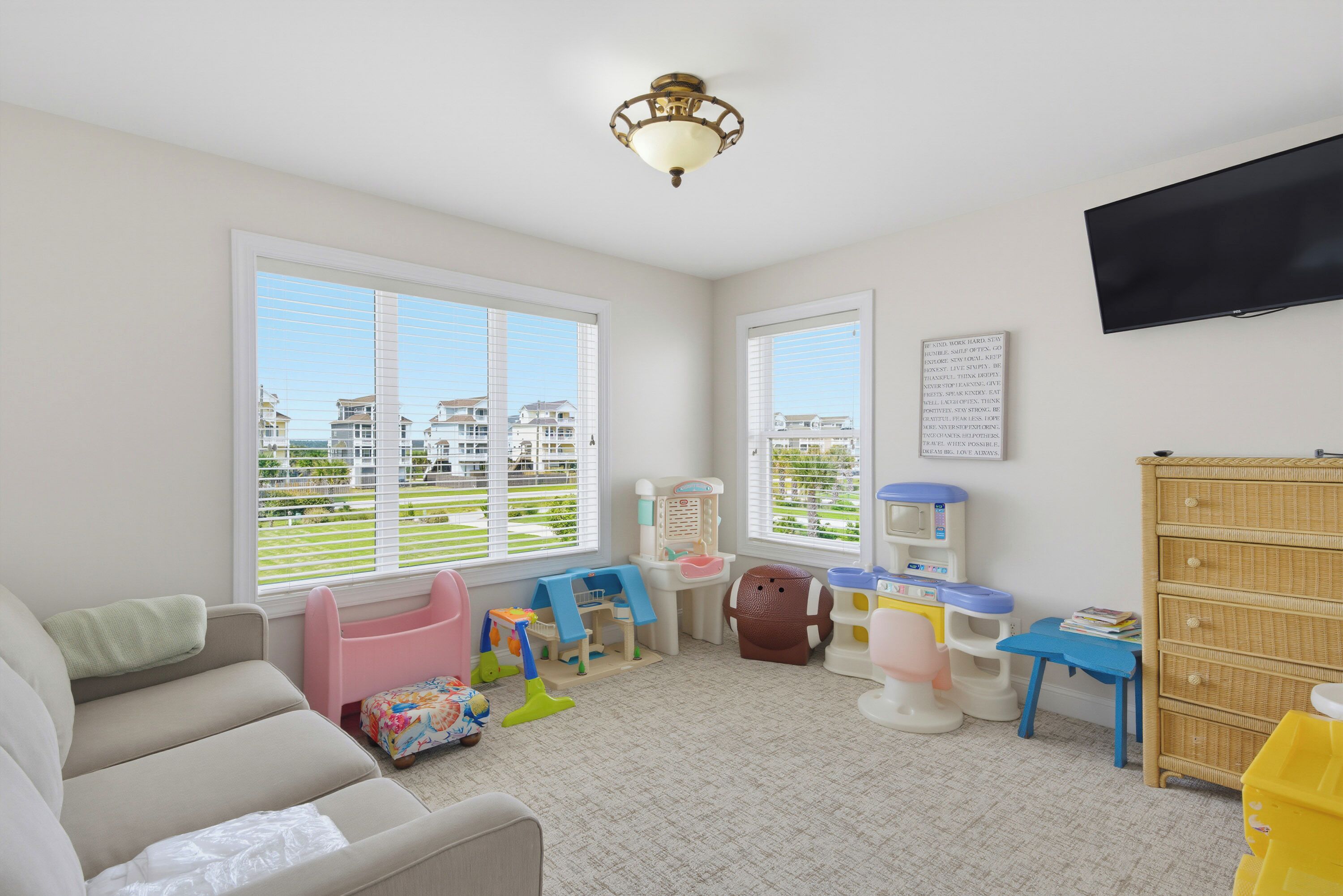 A well-lit room with a large window, a ceiling fan, a television, and a crib.