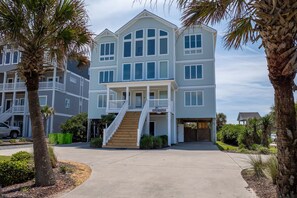 A multi-story residential building with a central staircase, a covered garage, and a landscaped driveway. - Oceanfront pool and pirate playhouse (North Topsail Beach)