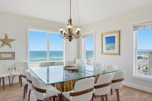 A dining area with a glass table surrounded by chairs, large windows with ocean views, a star decoration, and a framed painting. - Oceanfront pool and pirate playhouse (North Topsail Beach)