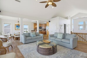 A spacious living area with two sofas, a glass coffee table, wicker ottomans, and a dining area with chairs and a table. - Oceanfront pool and pirate playhouse (North Topsail Beach)