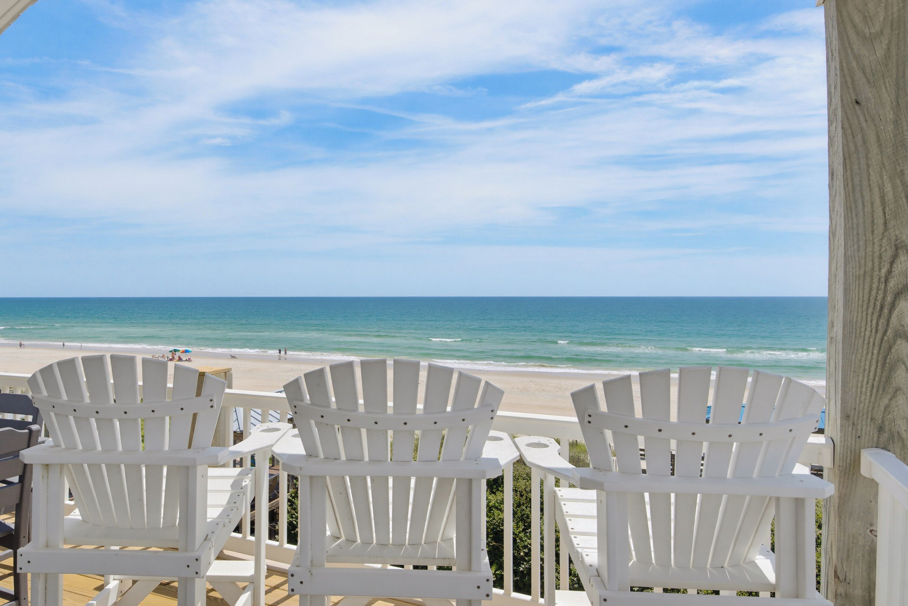 A beachside view with white Adirondack chairs and a wooden deck overlooking the ocean.