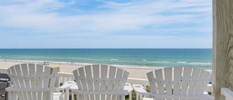 A beachside view with white Adirondack chairs and a wooden deck overlooking the ocean.