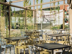 Un área de estar al aire libre con mesas y sillas, rodeada de paredes de vidrio con vegetación.