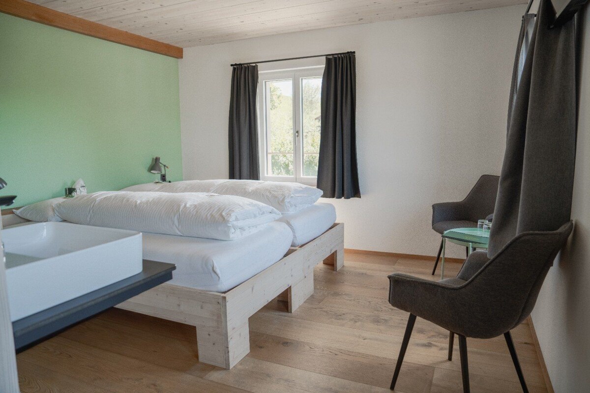Un dormitorio con cama, una silla, una ventana y un lavamanos.