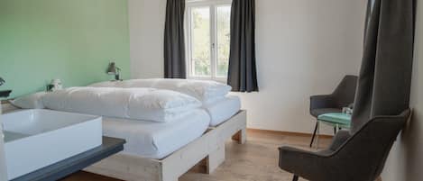 A bedroom with a bed, a chair, a window, and a sink.